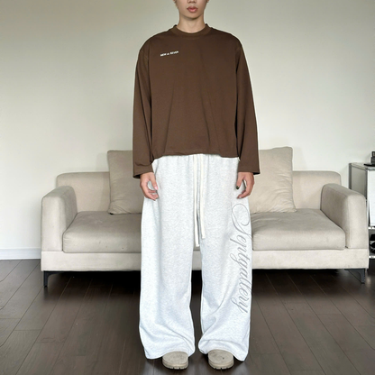 Person wearing a brown long-sleeve shirt and white pants standing in a living room.