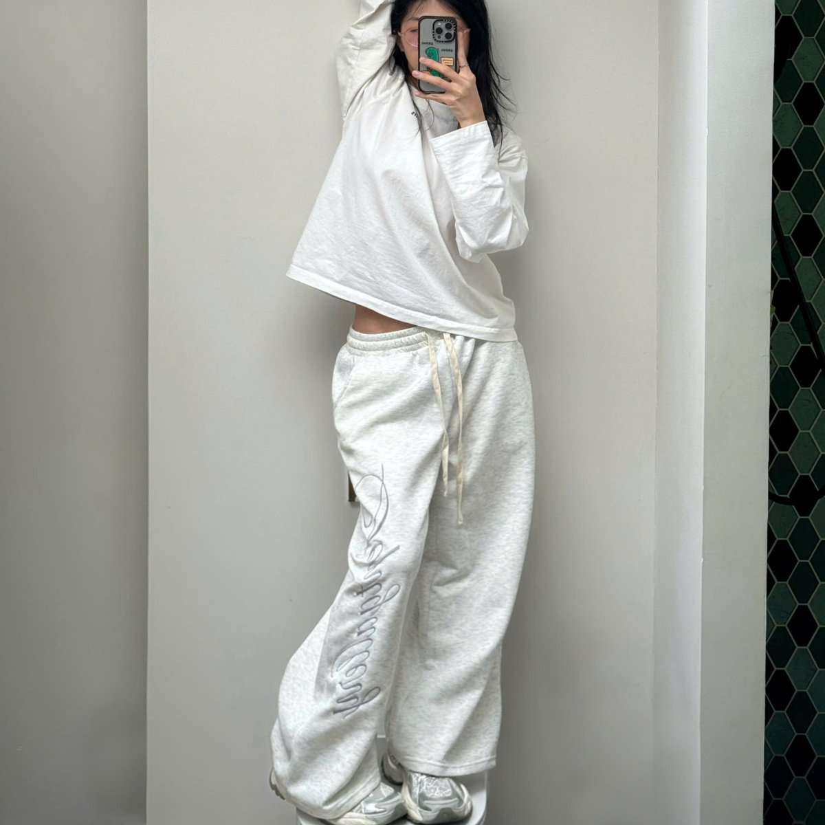 Person wearing a white tracksuit standing against a plain wall.