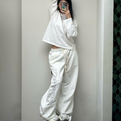 Person wearing a white tracksuit standing against a plain wall.