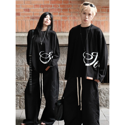 Two people wearing black outfits with white designs against a brick wall.