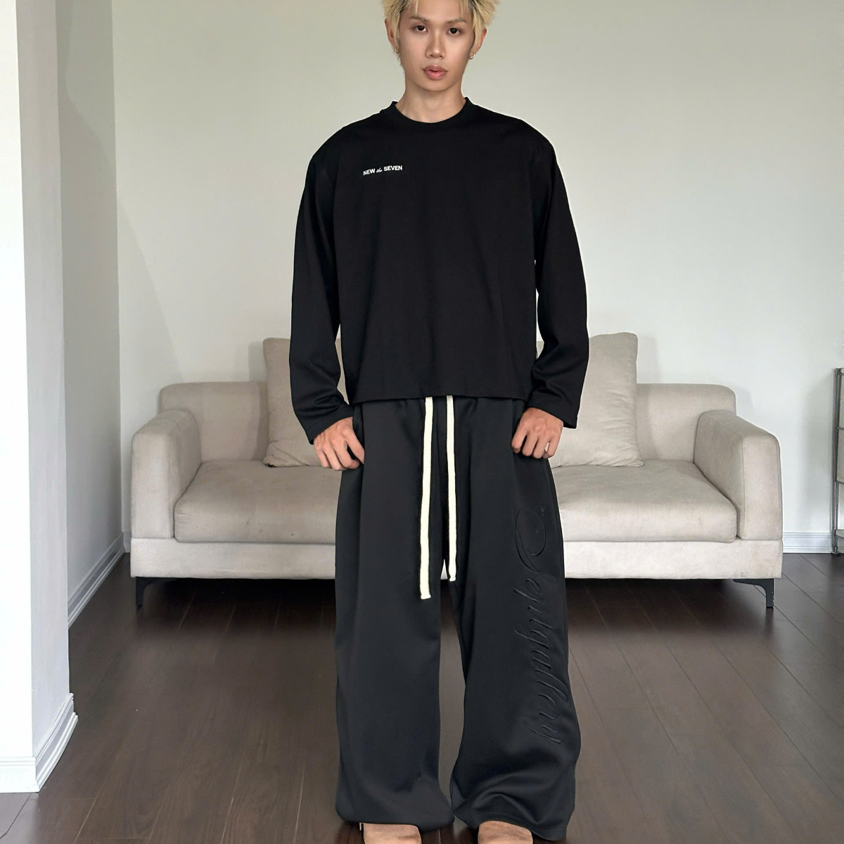 Person wearing a black outfit in a minimalistic room with a beige sofa.